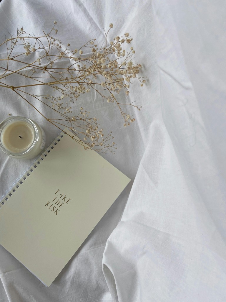 Libreta con la frase Take the risk, una vela y flores secas: símbolo de empezar terapia